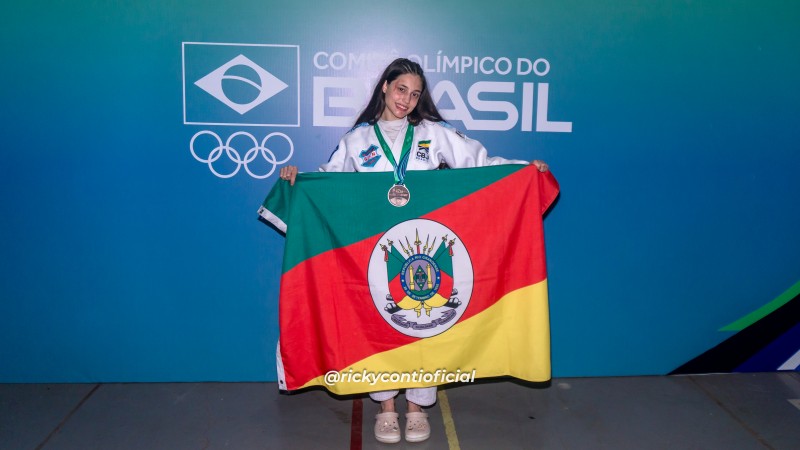 Jovem posa com medalha e bandeira do Rio Grande do Sul