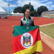 Jovem posa com bandeira do Rio Grande do Sul com pista de atletismo ao fundo